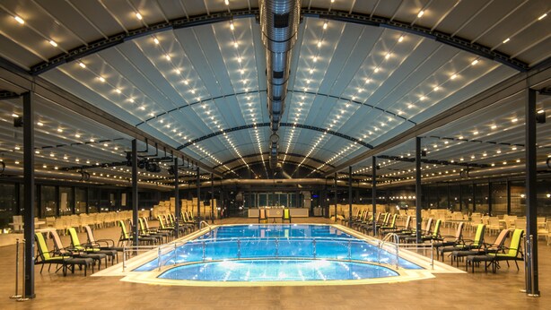 A large indoor swimming pool with a high ceiling and numerous lights, surrounded by rows of lounge chairs. - Babillon Hotel Spa & Restaurant (Iyidere)