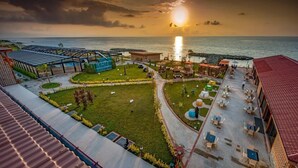 A coastal hotel with a patio area, outdoor seating, and a view of the ocean at sunset. - Babillon Hotel Spa & Restaurant (Iyidere)