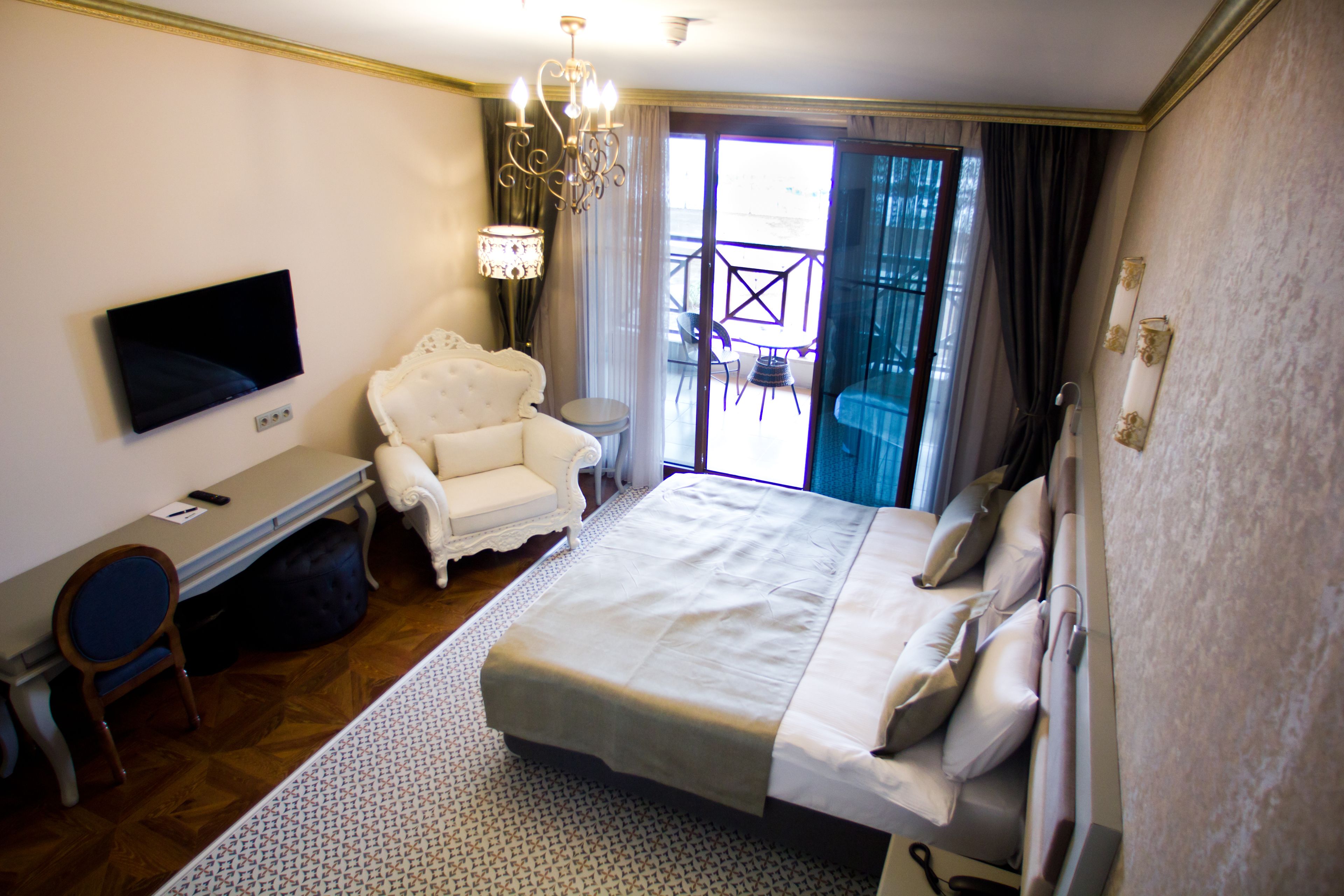 Una habitación de hotel con cama, escritorio con televisor, silla y balcón con mesa y sillas.