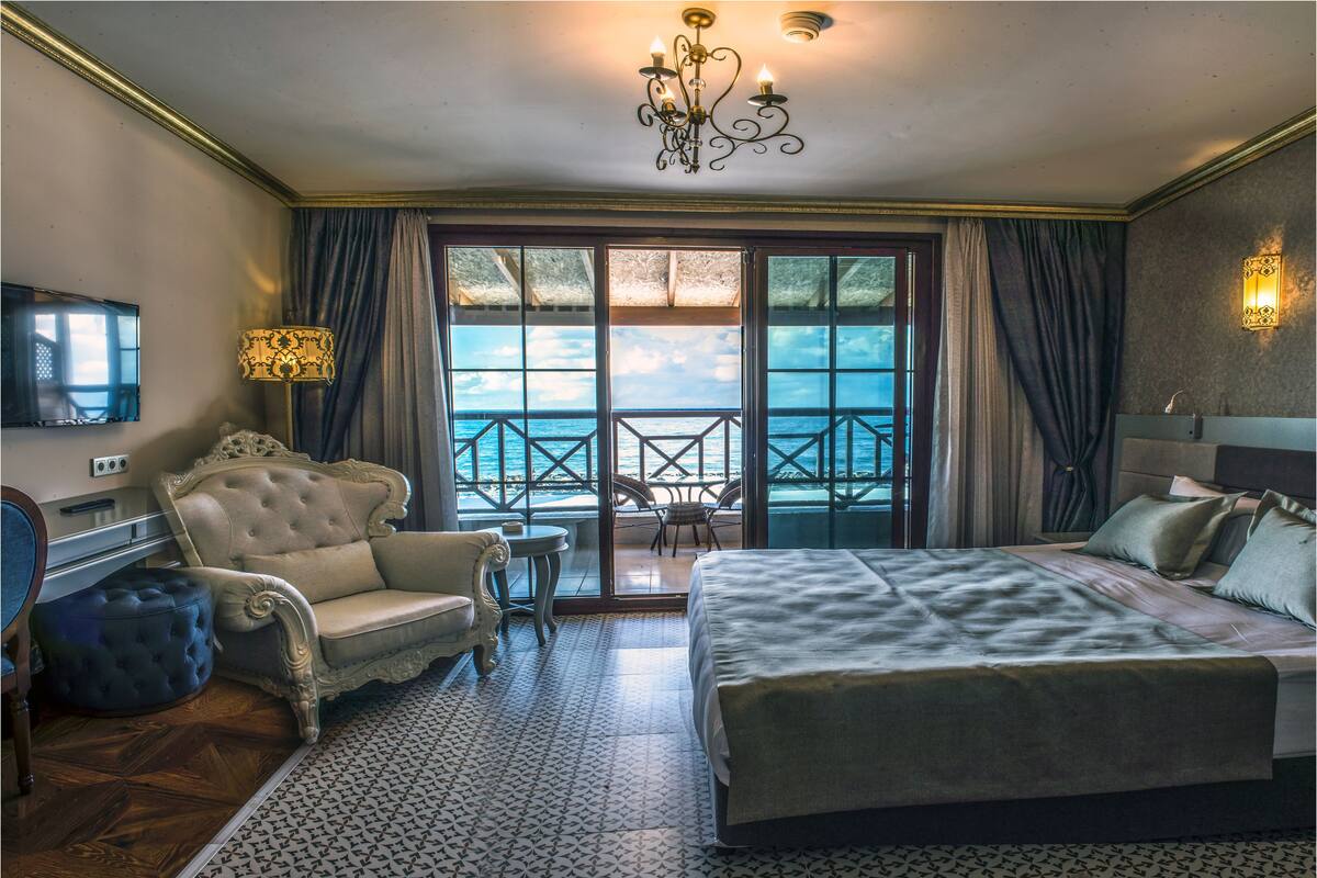 Une chambre d’hôtel avec un grand lit, un canapé, une télévision et un balcon donnant sur la mer.