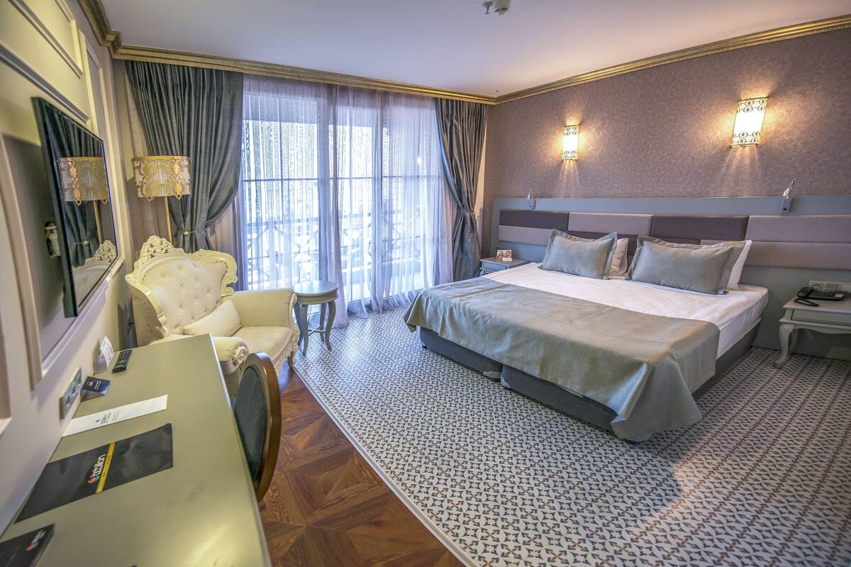 Une chambre d’hôtel avec un grand lit, un bureau, une chaise et une fenêtre avec des rideaux.