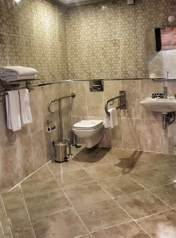 Baño con inodoro, lavamanos y barras de apoyo.