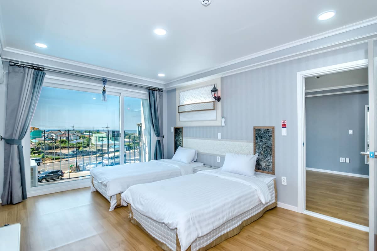 A hotel room with two beds, a large window with curtains, a view of the outside, and a door to a closet.