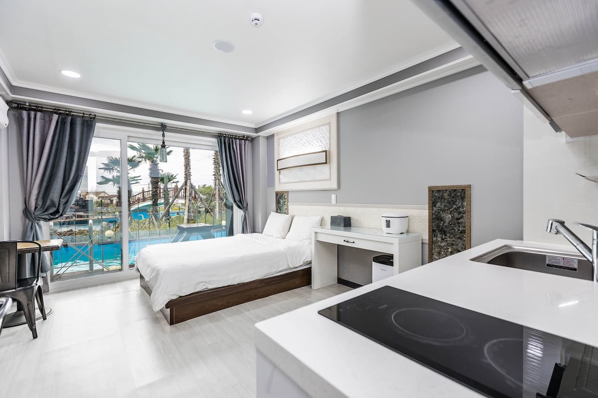 A modern hotel room with a bed, desk, and kitchenette.