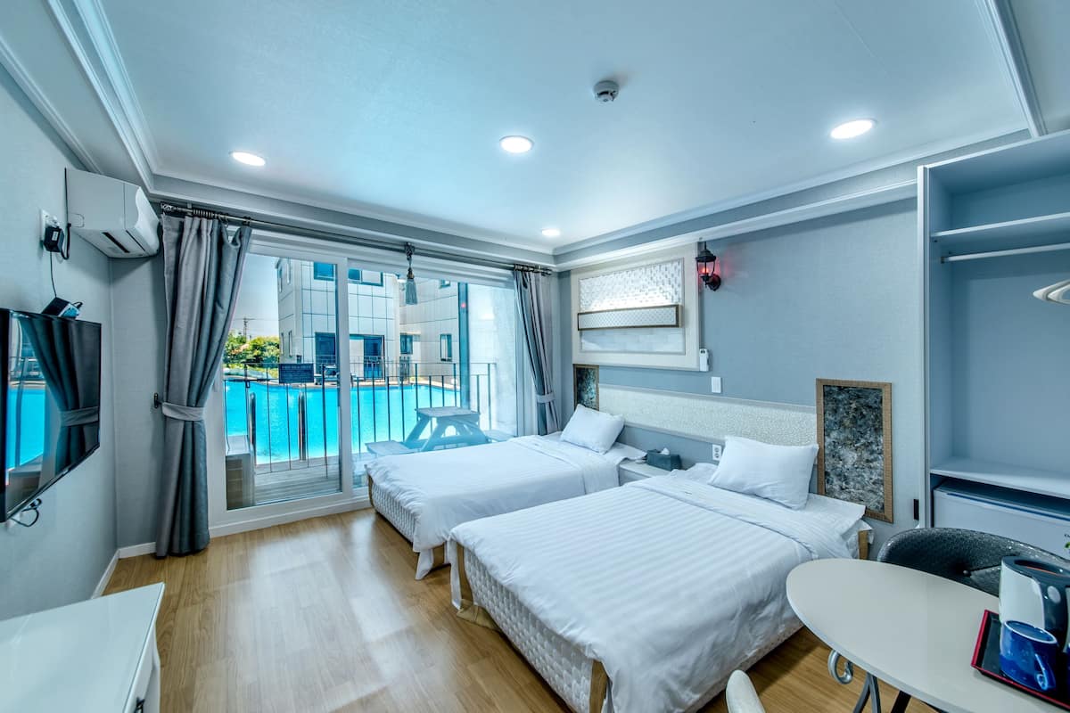 A hotel room with two beds, a TV, a table, and a view of a swimming pool.