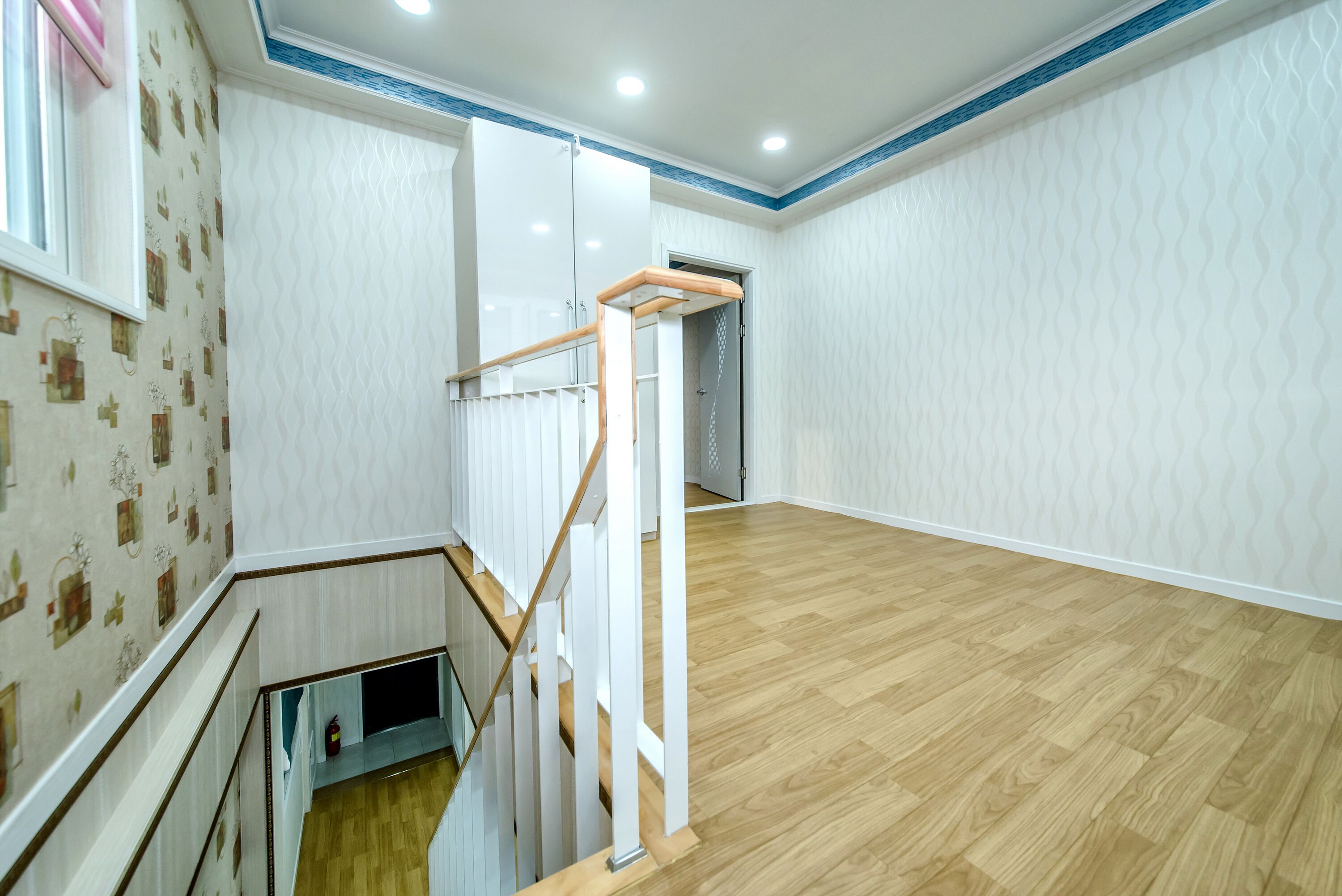 A spacious room with a wooden floor, white walls, and a staircase with a glass railing.