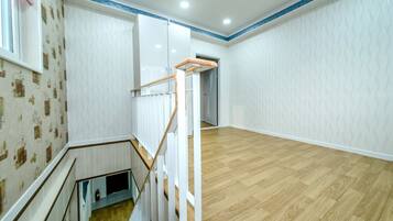 A spacious room with a wooden floor, white walls, and a staircase with a glass railing.