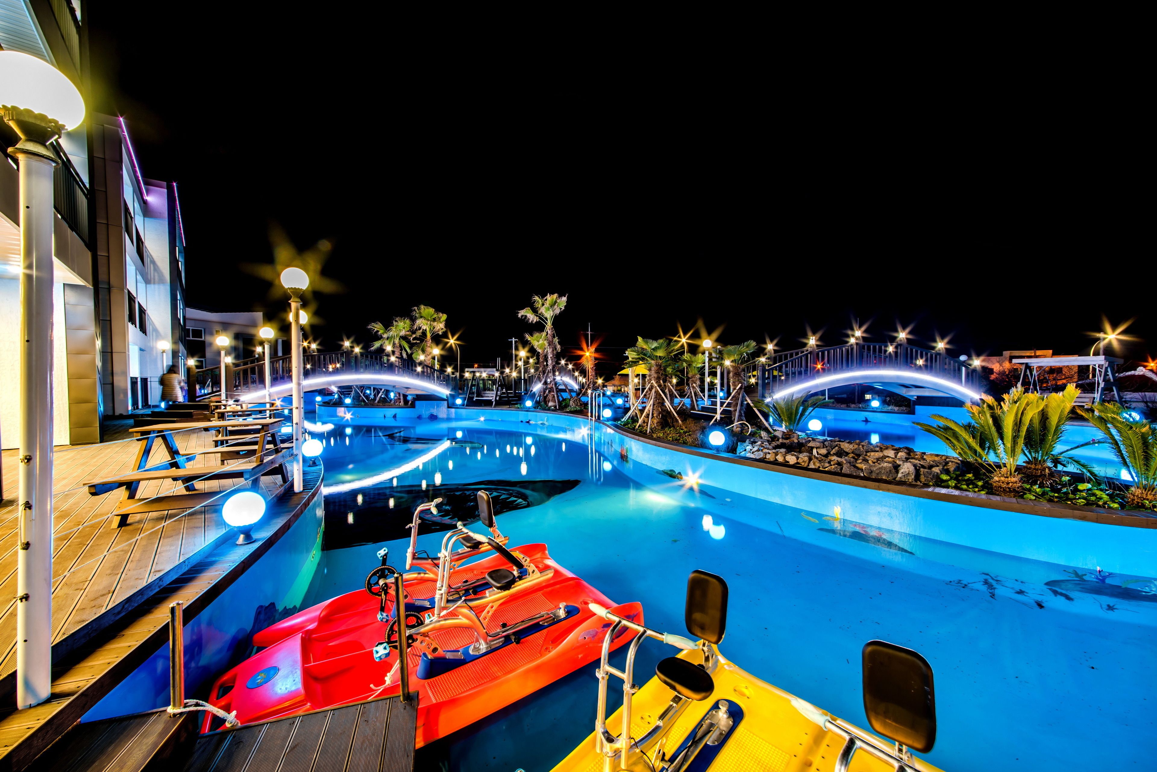 Área de piscina à noite, com várias pistas, uma boia inflável vermelha e um deck de madeira com bancos.