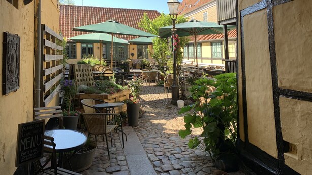 Un café en plein air avec un sol en pierre, des meubles en bois et des parasols verts.