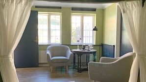 Une pièce avec deux chaises, une table sur laquelle se trouvent divers objets, et de grandes fenêtres avec des rideaux.