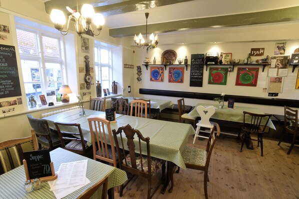 A restaurant interior with wooden tables and chairs, a chandelier, and various wall decorations. - Hotel Postgaarden (Ribe)