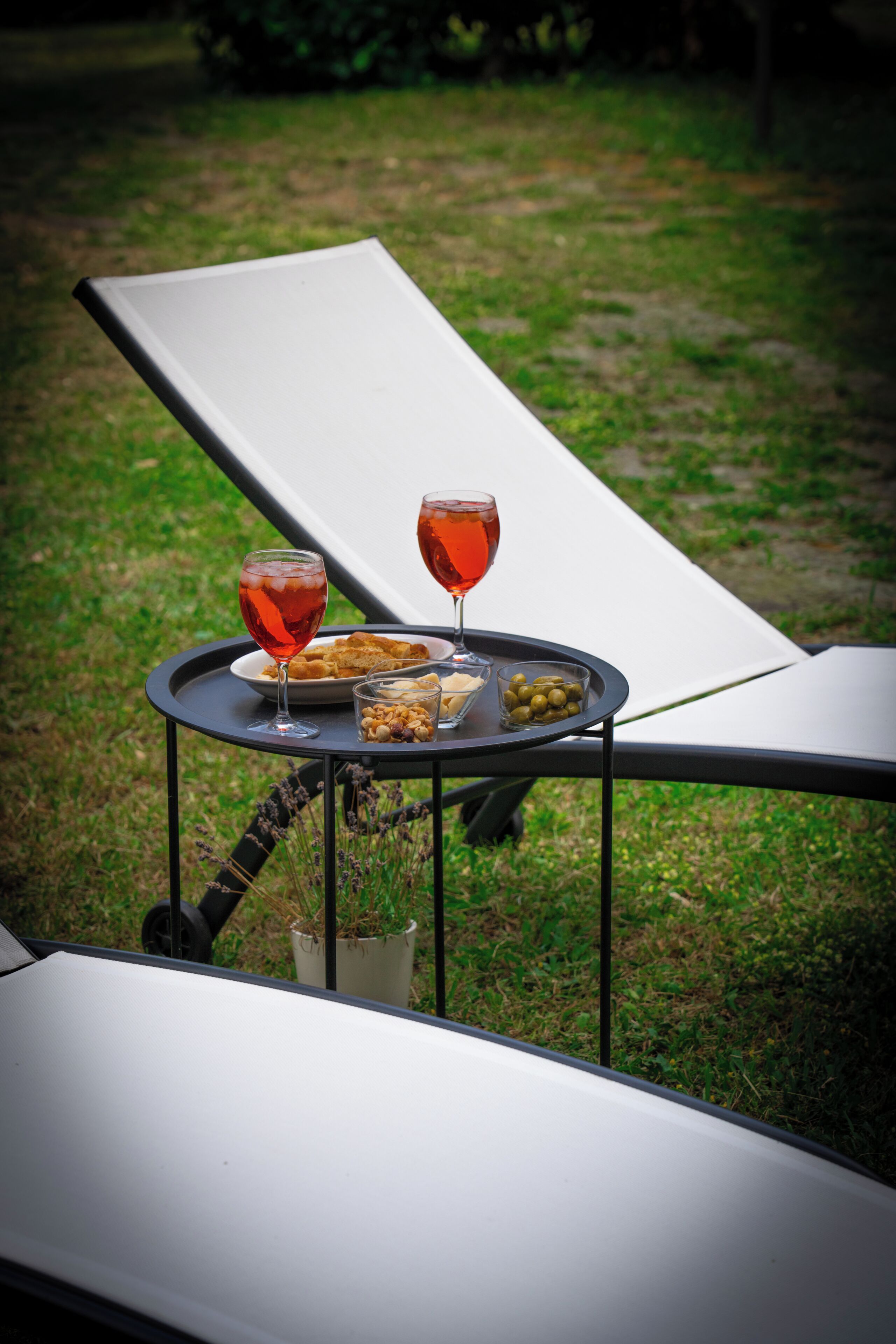 Un fauteuil confortable avec une petite table d’appoint sur laquelle se trouvent un verre d’une boisson rouge, une assiette de nourriture et un petit bol d’olives.