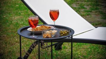 Un fauteuil confortable avec une petite table d’appoint sur laquelle se trouvent un verre d’une boisson rouge, une assiette de nourriture et un petit bol d’olives.