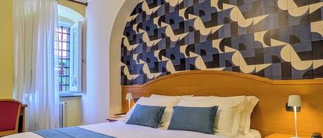 A hotel room with a bed, a nightstand, a lamp, a chair, and a window with curtains.