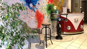Un espace d’accueil agrémenté d’un mur décoré d’une œuvre abstraite aux couleurs vives, d’un comptoir aménagé à partir d’un vieux combi Volkswagen, d’un tabouret de bar et d’une plante en pot.