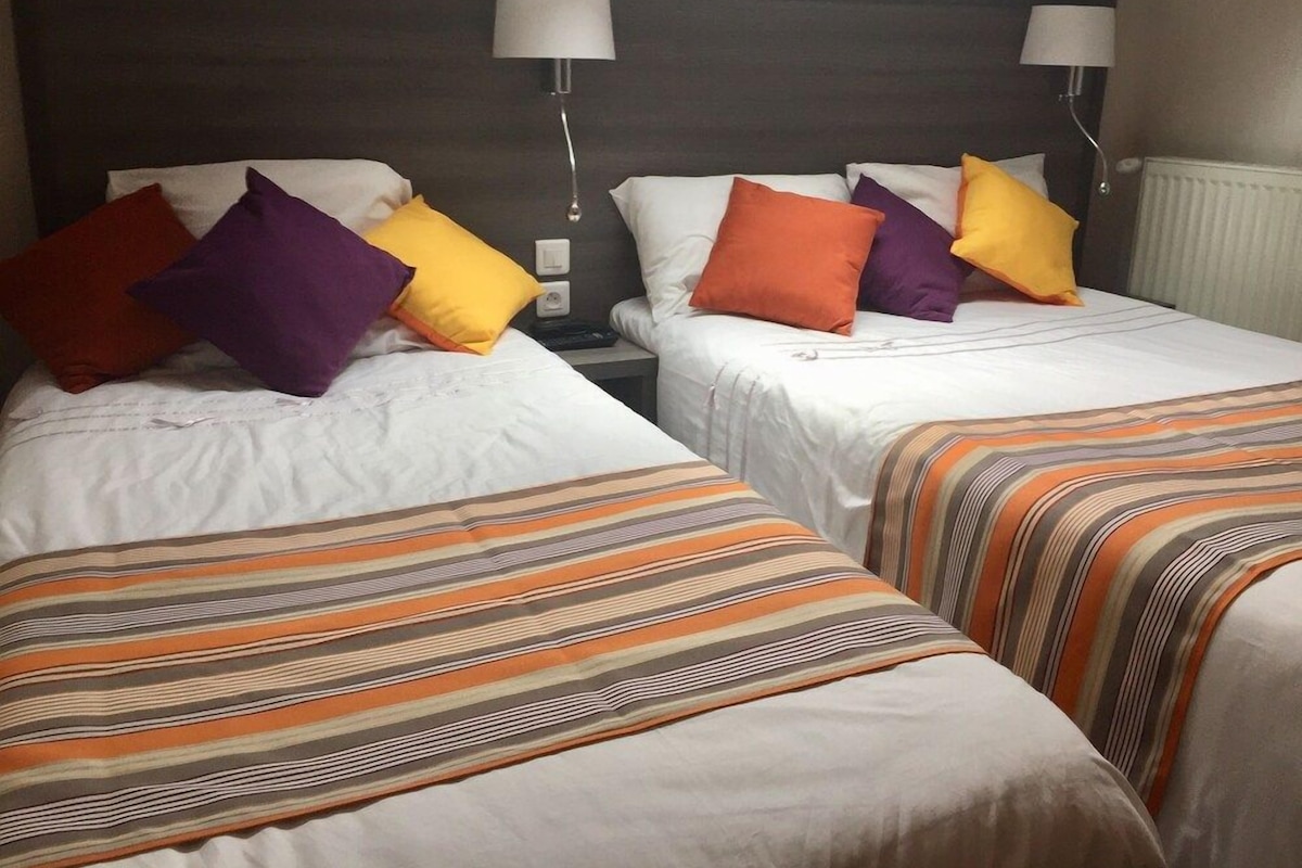 Een hotelkamer met twee bedden, elk met een ander beddegoed en twee nachtlampjes.