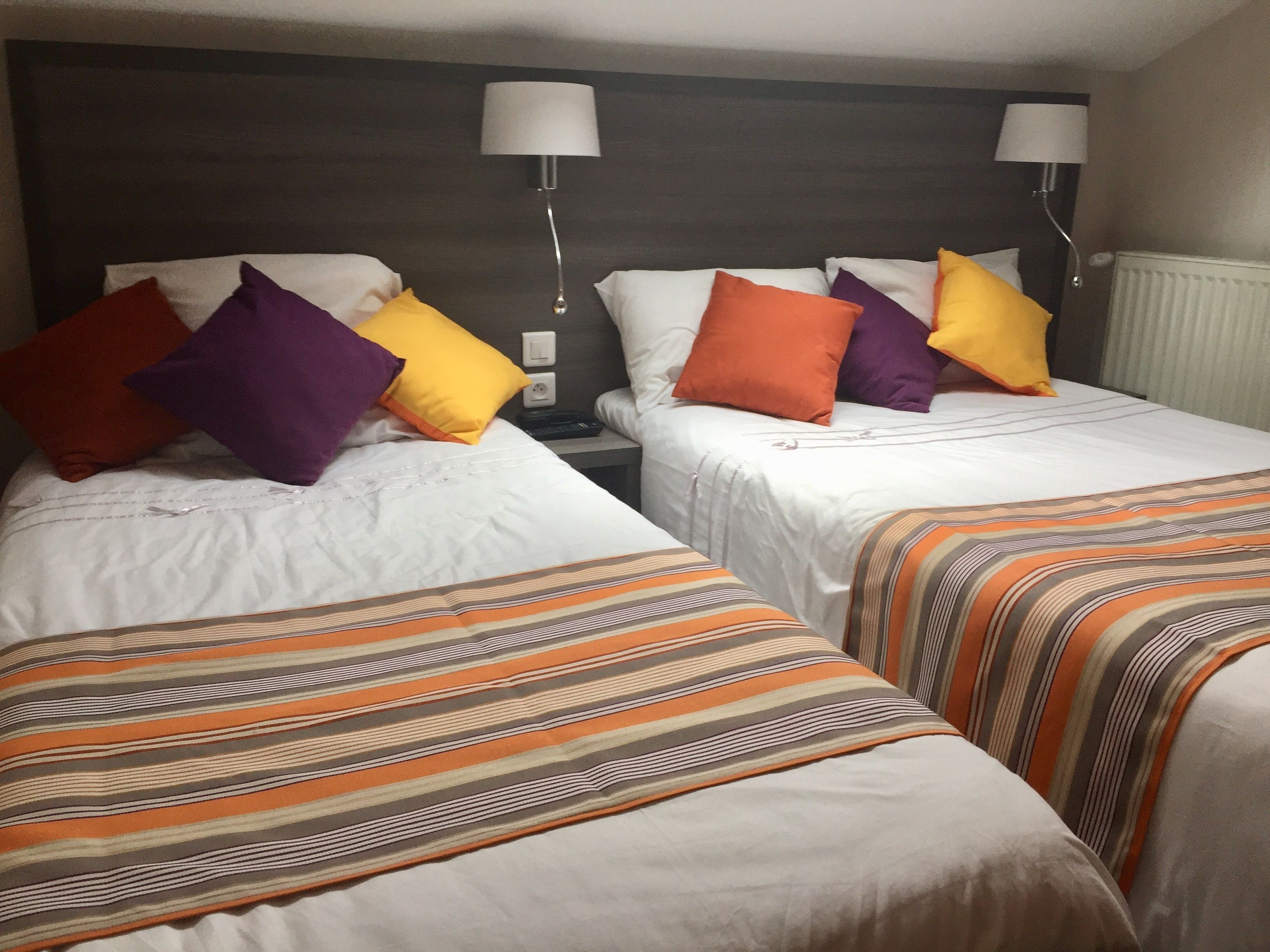 Dos camas individuales con ropa de cama a rayas, un cabecero oscuro y dos lámparas de noche.