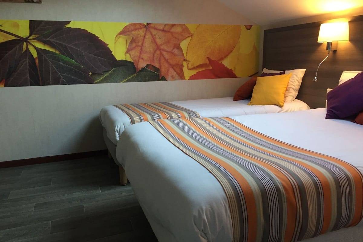 Une chambre d’hôtel avec un lit, un mur décoré de feuilles d’automne, une lampe de chevet et un plancher en bois.