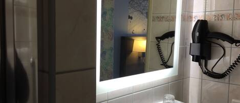 A bathroom with a mirror, a hairdryer mounted on the wall, and a sink with two glasses on it.