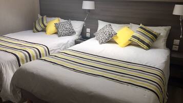 A hotel room with two beds, each with striped bedding and multiple pillows. There are bedside lamps and a nightstand with a lamp.