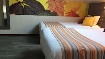 A hotel room with a bed, a striped pillow, a wall with autumn leaves, and a dark wooden floor.