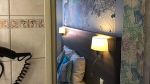 Une chambre d’hôtel comprenant un lit, deux lampes fixées au mur, une tête de lit décorative et un espace douche.