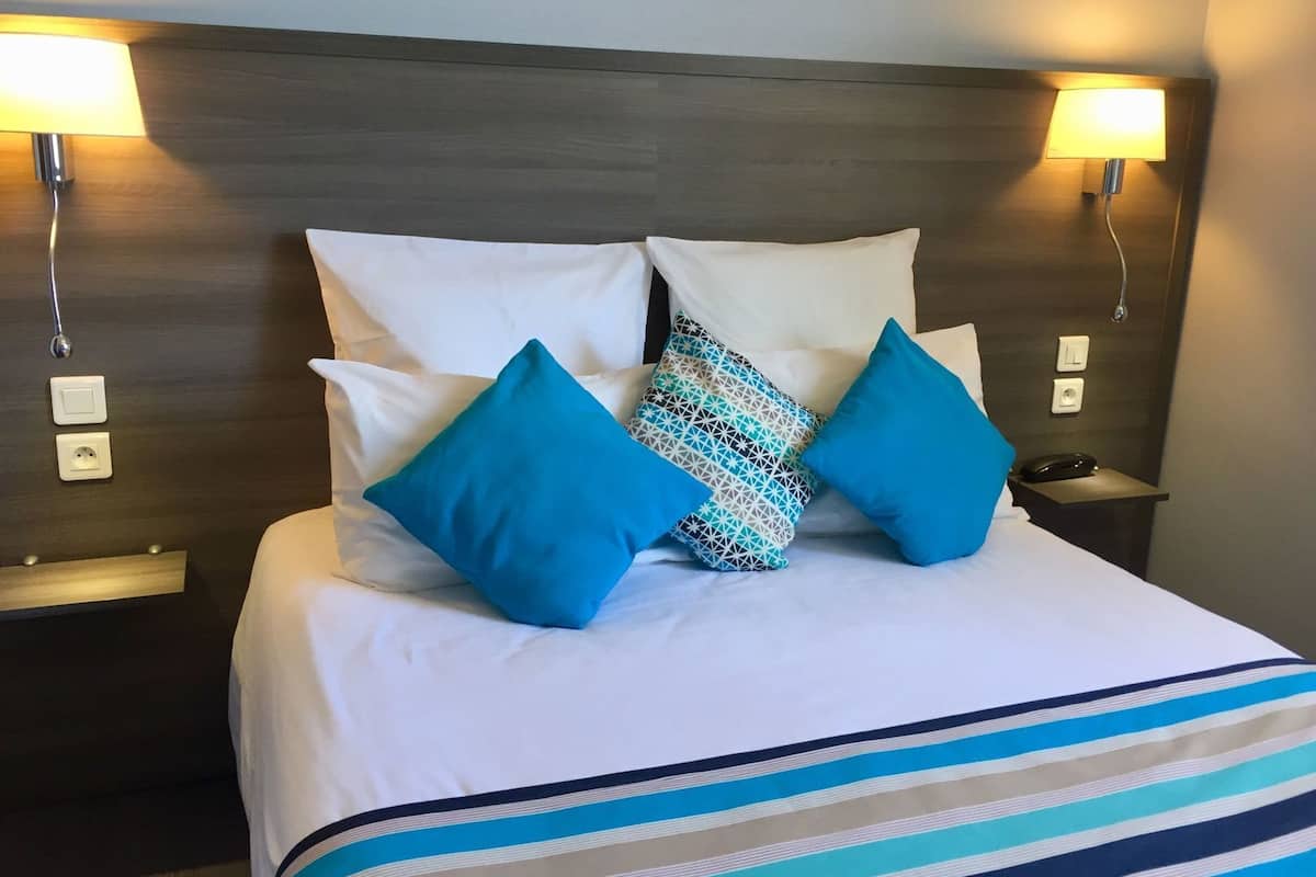 Une chambre d’hôtel avec un lit, deux lampes de chevet, un téléphone et une prise électrique sur la table de chevet.
