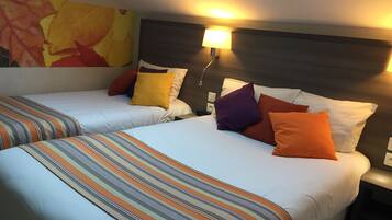 A hotel room with two beds, each with striped bedding and multiple pillows. There is a skylight above the beds, and a wall-mounted lamp on the nightstand.