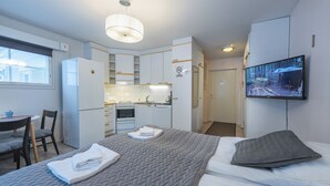 Quarto de hotel compacto com cama, televisão, kitchenette e área de refeições.