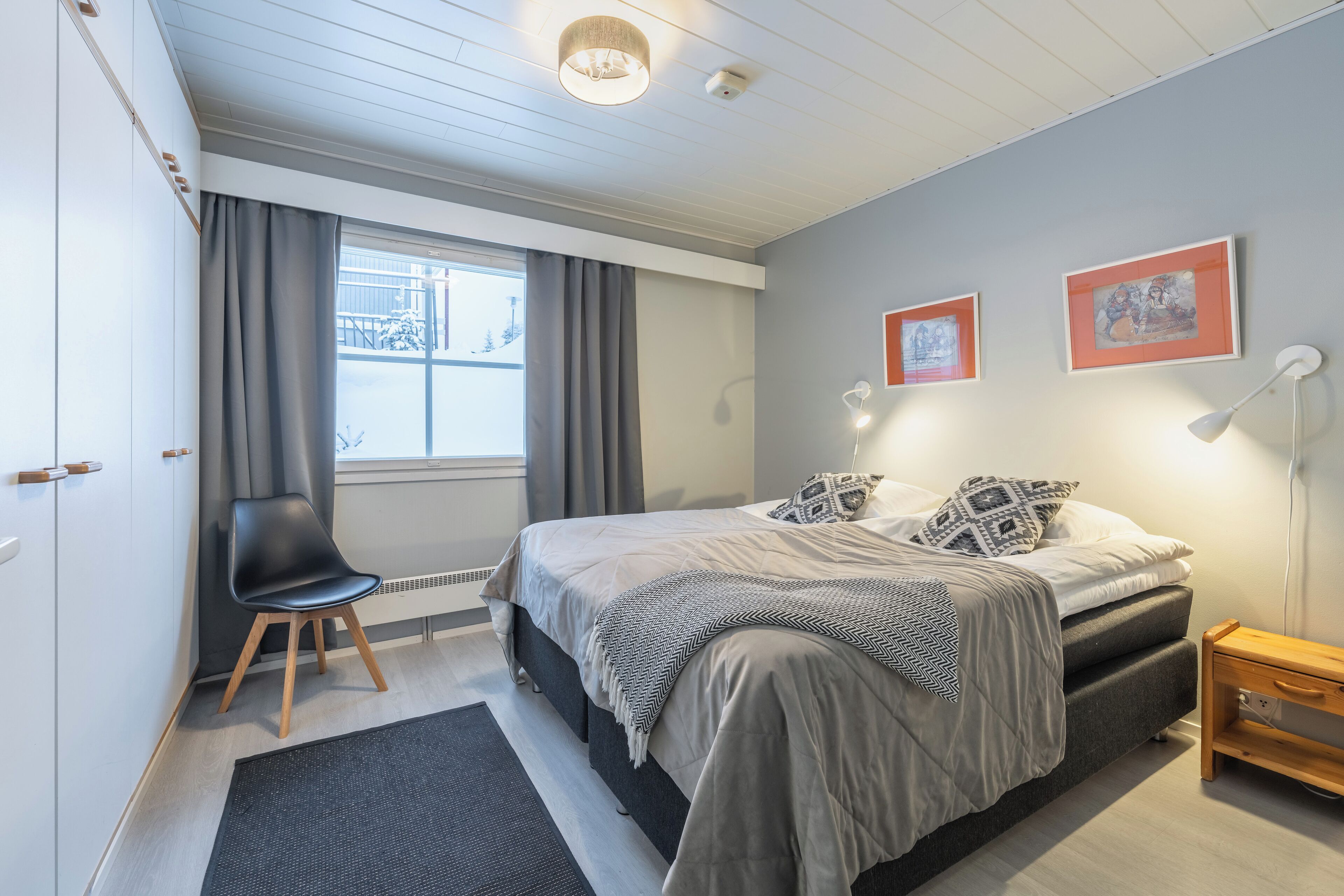 Un dormitorio moderno con cama, una silla, una mesita de noche y una ventana con cortinas.