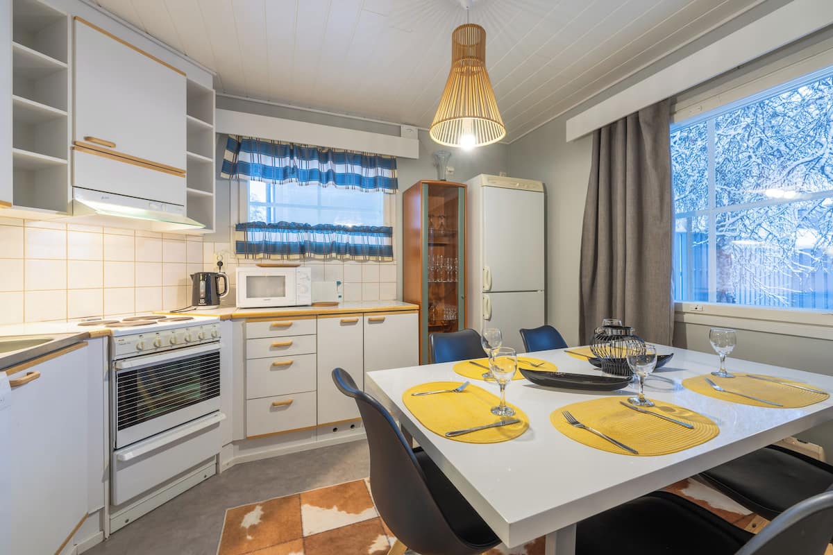 Een moderne keuken met witte kasten, een eettafel gedekt met gele placemats en een raam met uitzicht op besneeuwde bomen.
