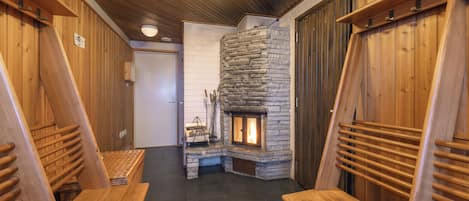 A wooden interior with a stone fireplace, benches, and a door.
