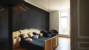 A modern bedroom with a bed, bedside tables, a hanging light fixture, and a view of the outdoors through a window. - Boutique Apartments - Main Market Square (Kraków)