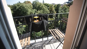A balcony with wicker furniture, a small table, and a view of trees and buildings. - Boutique Apartments - Main Market Square (Kraków)