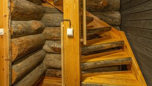 Una escalera espiral de madera en el interior de una cabaña de troncos, con una puerta de madera y un interruptor de luz en la pared.