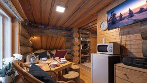 Interior acogedor de una cabaña de troncos con una mesa de comedor de madera dispuesta para dos personas, un televisor montado en la pared y un refrigerador en la esquina.