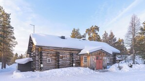 Una cabaña de troncos con techo nevado, rodeada de árboles.