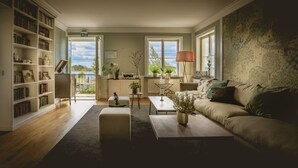 A living room with a sofa, coffee table, and bookshelves. There is a view of the outdoors through a door. - Almåsa Havshotell (Vasterhaninge)