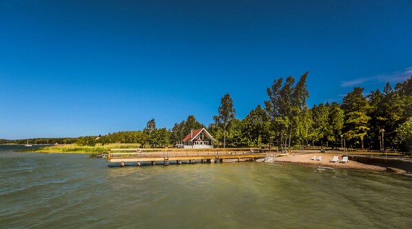 A lakeside cabin with a dock extending into the water, surrounded by trees and a clear sky. - Almåsa Havshotell (Vasterhaninge)