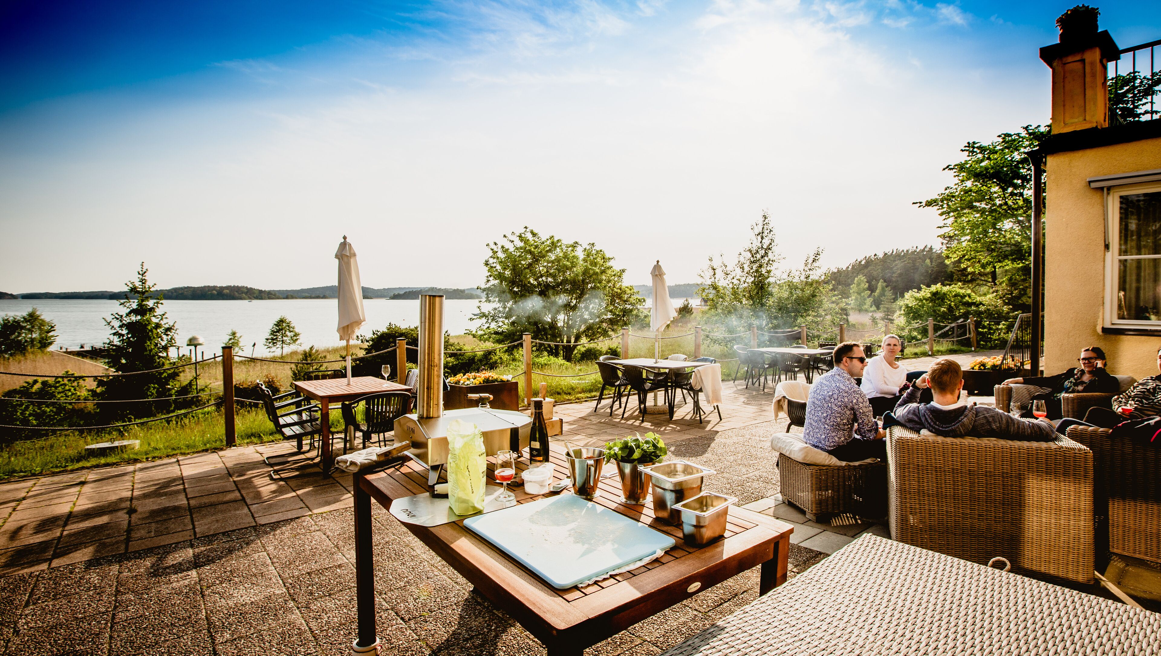 An outdoor patio with tables and chairs, a grill, and a view of a lake.