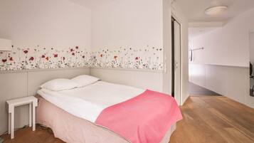 A bedroom with a bed, a nightstand, a pink blanket, and a wall with a floral design.