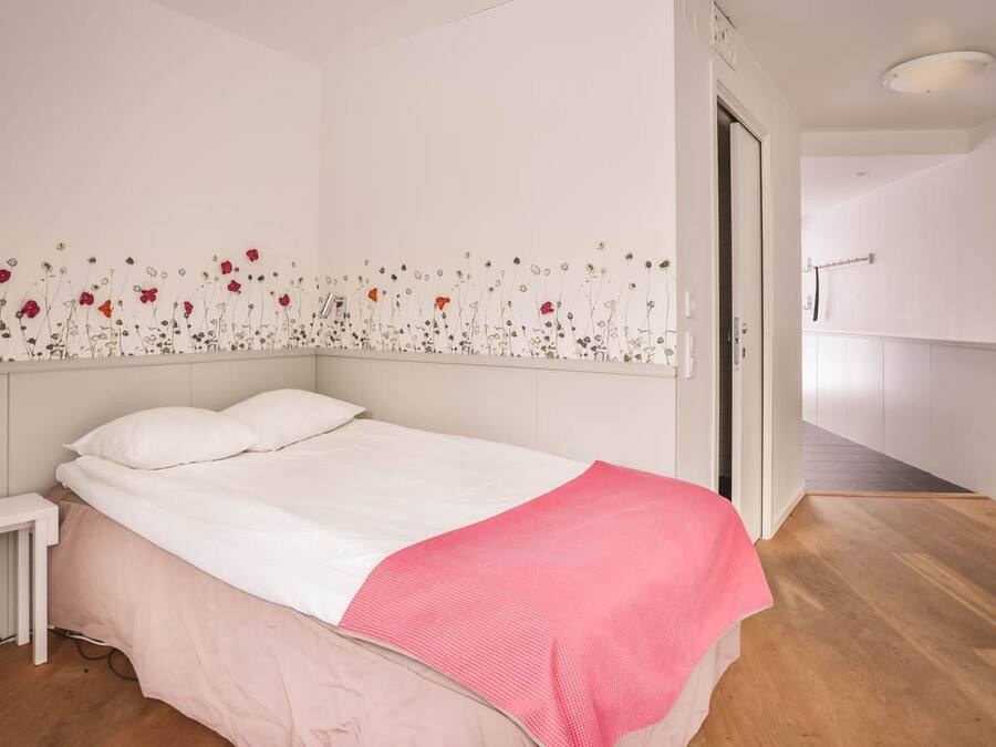 A bedroom with a bed, a nightstand, a pink blanket, and a wall with a floral design.