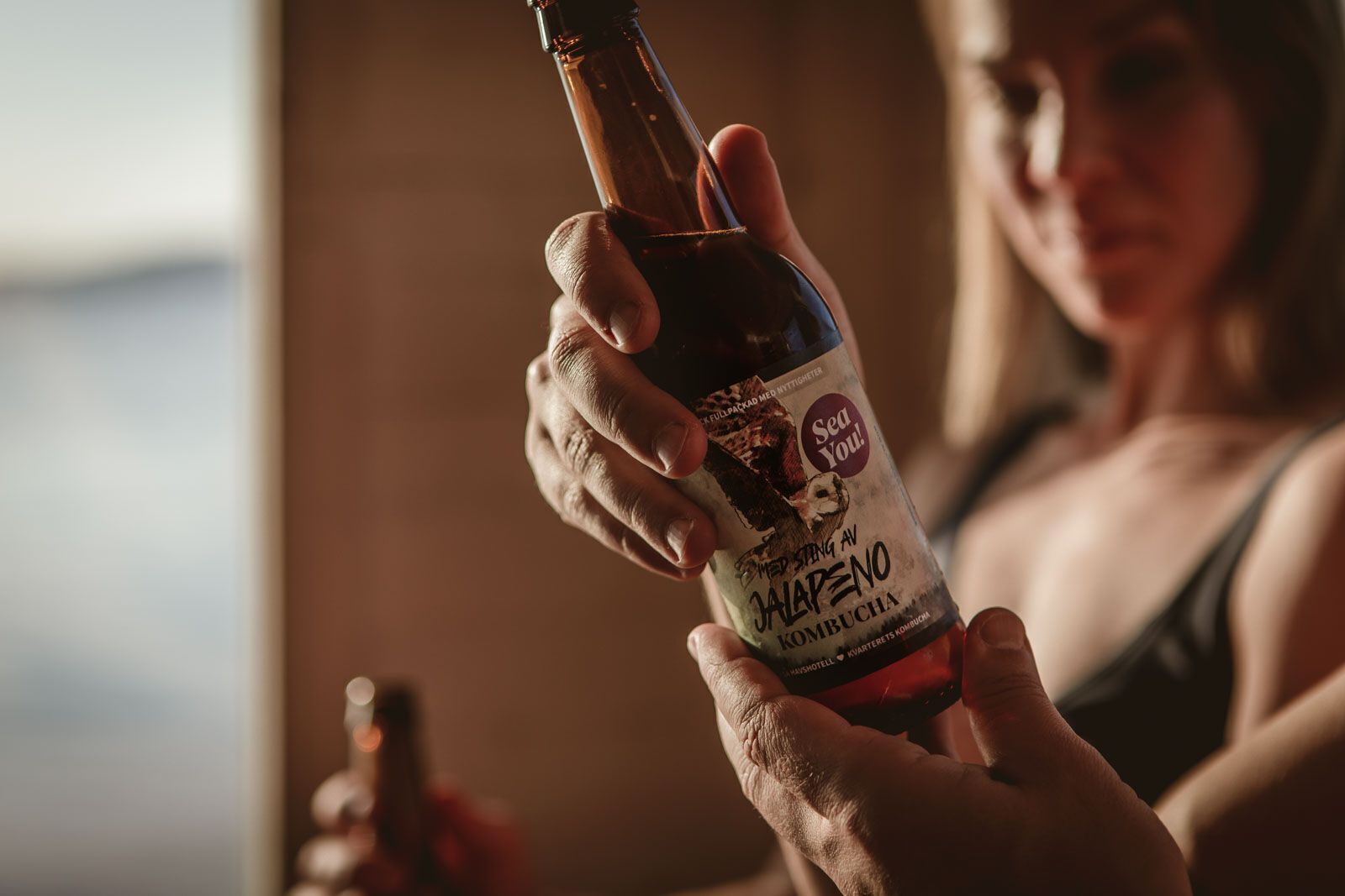 A person holding a bottle of 'Sea You! Hoppang Av Jalapeno Kombucha'.