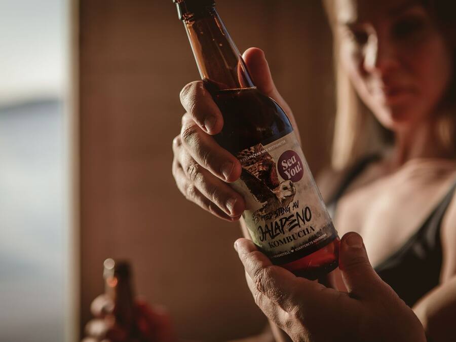 Una persona sosteniendo una botella de 'Sea You! Hoppang Av Jalapeno Kombucha'.