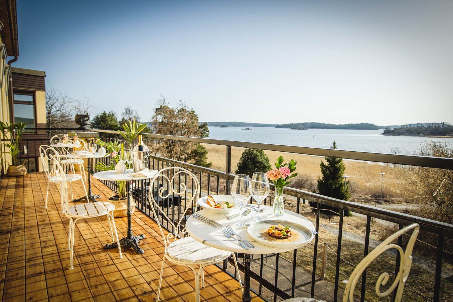 A terrace with tables and chairs, overlooking a body of water and hills.