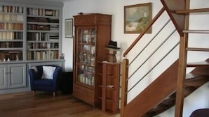 Una habitación con una escalera de madera, una estantería, un sillón azul y un armario.