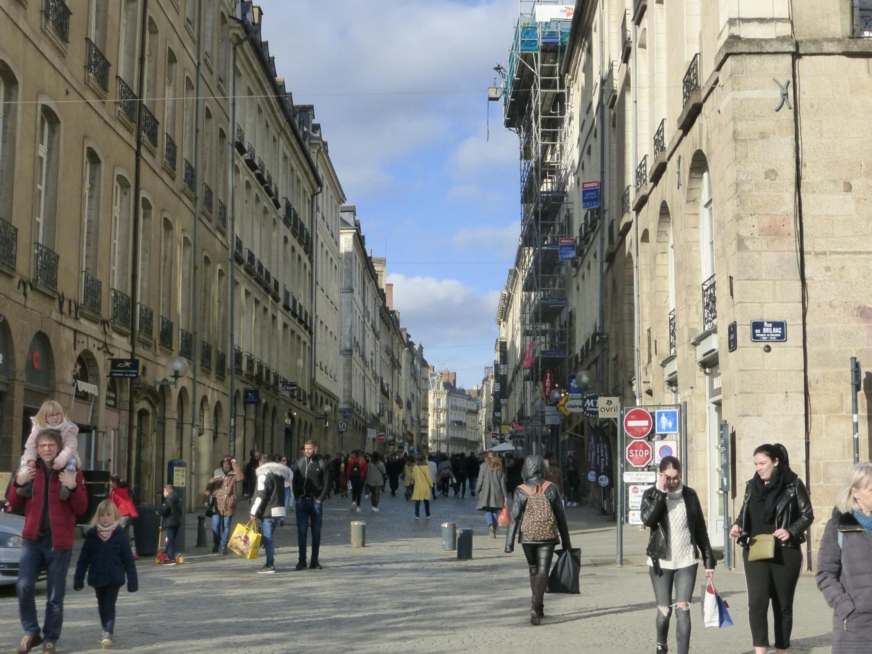 Une rue animée en milieu urbain, avec des piétons, des bâtiments historiques et des enseignes commerciales.