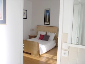A bedroom with a wooden bed, white bedding, a nightstand with a lamp, and a framed picture on the wall. - Chambres de Condate (Rennes)