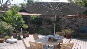 Un patio al aire libre con una mesa redonda, sillas de madera y un paraguas grande.
