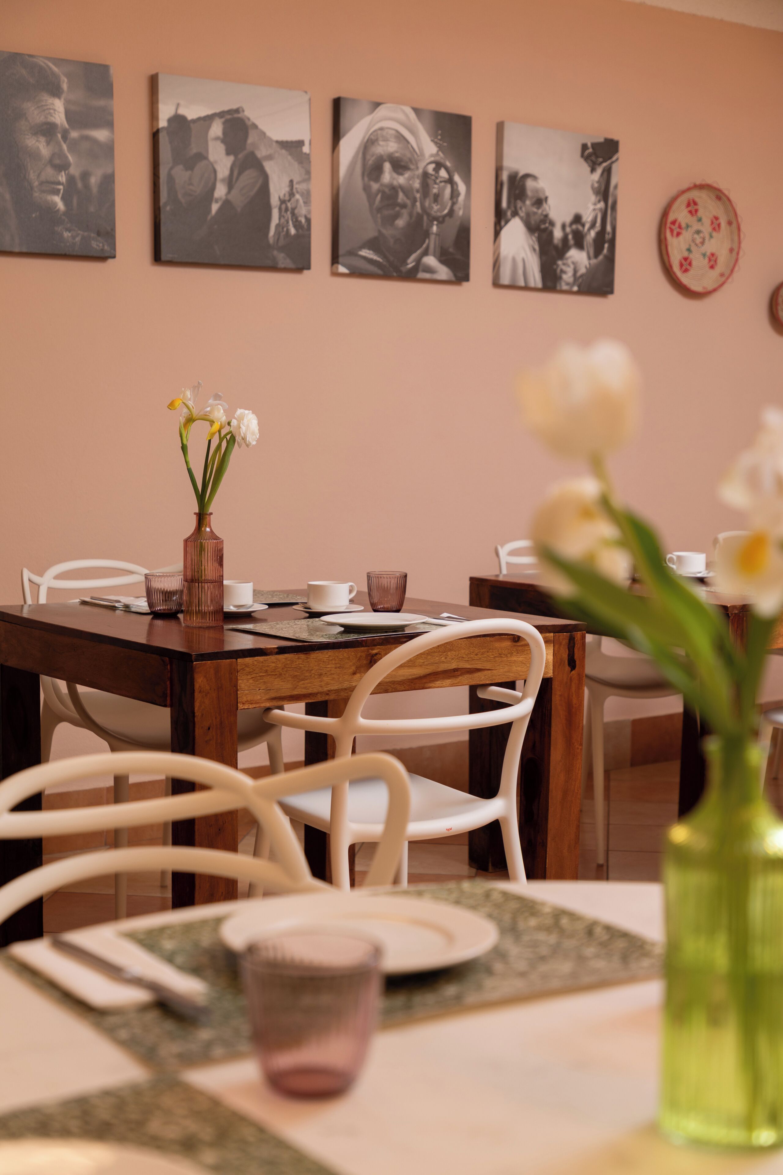 A dining area with a wooden table, white chairs, a vase with flowers, and framed photographs on the wall.